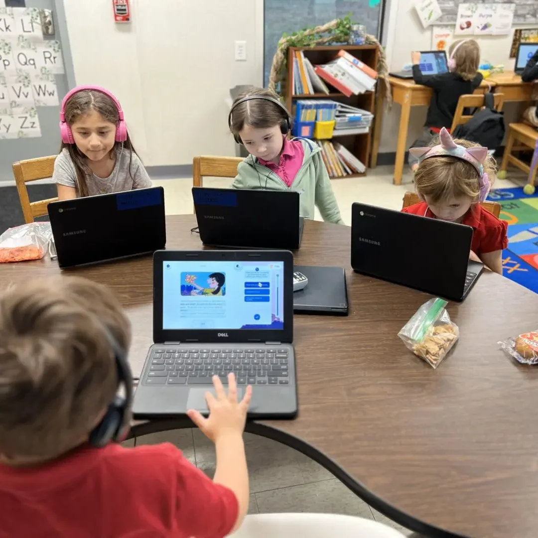 A group of children sitting at a table with laptops.