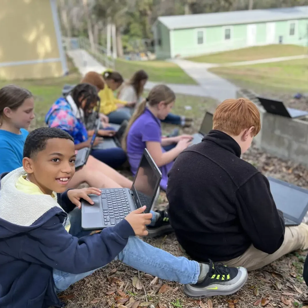 A group of kids sitting on the ground with laptops.